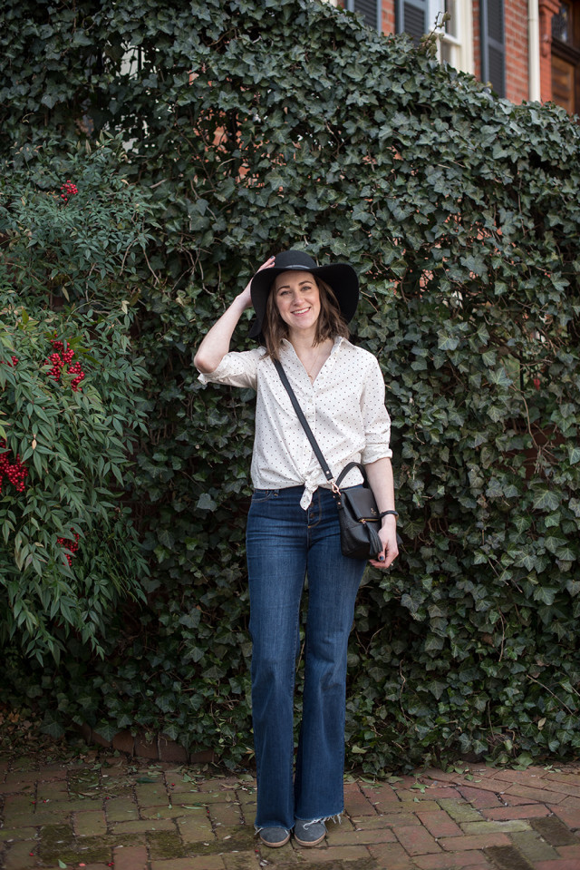 A polka dot shirt tied at the waist, flare jeans, and a black floppy hat for spring